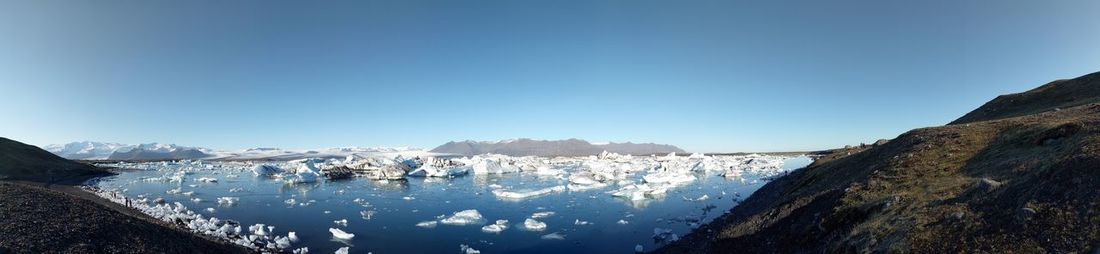 Panoramic view of ice floes in sea by mountains against blue sky