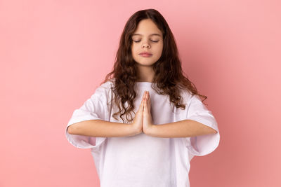 Portrait of young woman standing against pink background