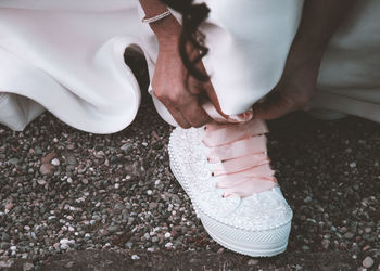 Low section of bride tying shoelace on field