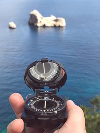 Close-up of hand holding clock against sea