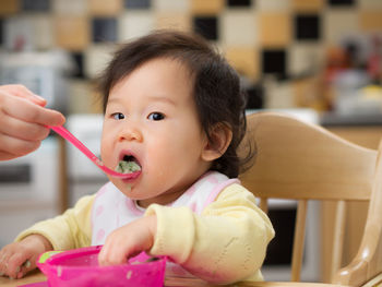 Close-up portrait of cute baby girl eating food at home