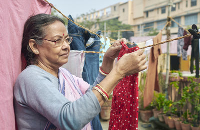 Portrait of a simple looking mature indian woman hanging freshly washed laundry to dry in the sun