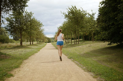 Rear view of woman jogging on footpath amidst field