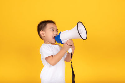 Full length of a boy standing against yellow background