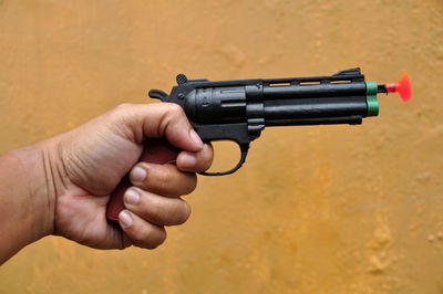 Cropped hand holding gun against yellow background