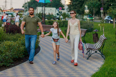 Family holding hands and walking on footpath