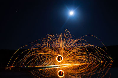 Man spinning wire wool at lakeshore during night