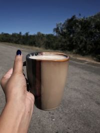 Holding a cup of coffee while standing on a quiet road. 