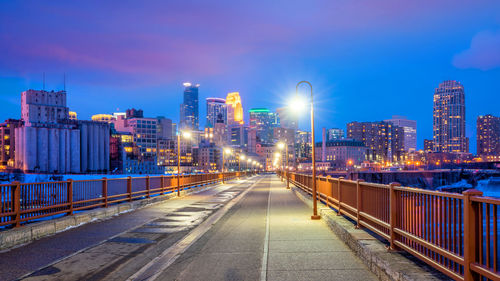 Illuminated street amidst buildings against sky at night