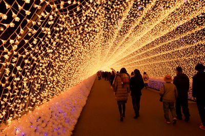 Rear view of people walking on illuminated street at night