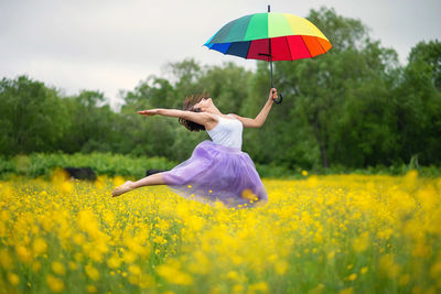 Woman with umbrella against yellow flowers on field