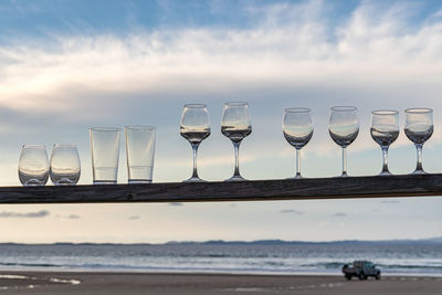 Row of wine glass on table at beach against sky