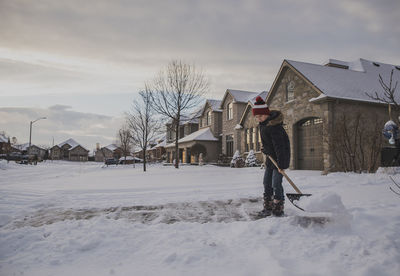 Boy removing snow using shovel against houses