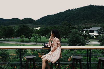 Side view of woman sitting on tree against sky