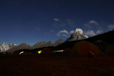 Tents by rocky mountains against sky at night