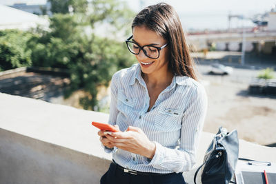 Happy businesswoman using smart phone leaning on wall
