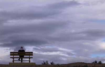 Rear view of man sitting on bench against cloudy sky. almeria, spain