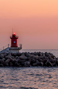 Lighthouse by sea against sky during sunset