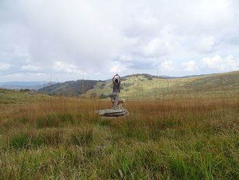 Rear view of woman exercising on rock against sky