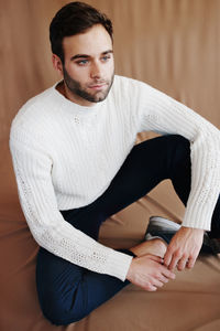 Full length of man sitting against beige background