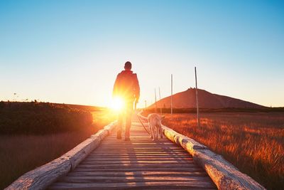 Rear view of man walking on road against sky during sunset