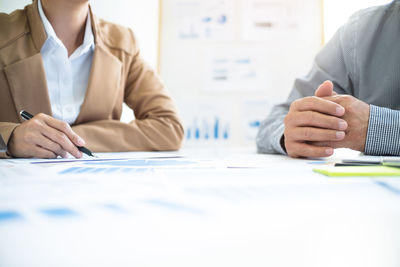 Midsection of colleagues analyzing chars on office desk