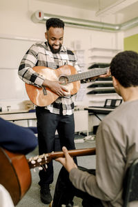 Male teacher playing guitar with students in music class at high school