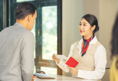 At the airport check-in counter, a passenger hands over his documents to the manager via a counter 