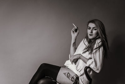 Portrait of woman smoking cigarette against gray background
