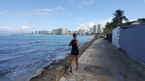 Rear view of man walking on retaining wall by sea against sky