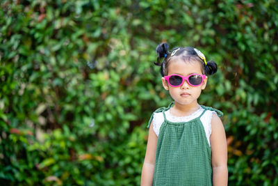 Portrait of girl wearing sunglasses standing against plants