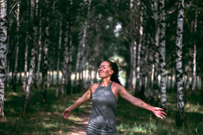 Smiling woman standing on land against trees in forest