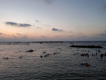 People swimming in sea against sky during sunset