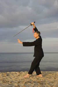 Man practicing tai chi at beach against cloudy sky