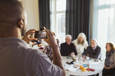 Male caregiver photographing senior men and women on smart phone in nursing home