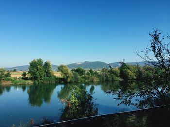 Scenic view of lake by trees against clear blue sky