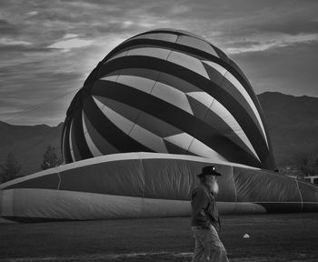 Side view of mature man with hands in pockets walking by hot air balloon on field