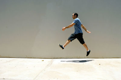 Side view of man levitating over sidewalk by wall