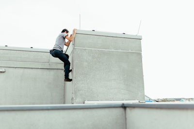 Low angle view of man climbing on building against clear sky