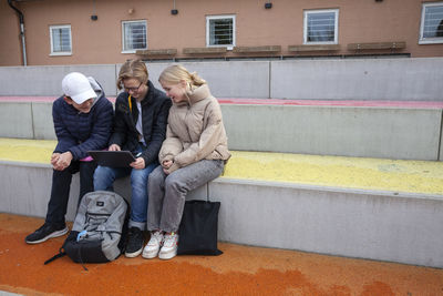 School friends sitting in front of school and using laptop