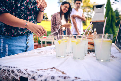 Midsection of woman standing by drinks on table with friends in background