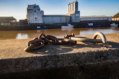 Rusty chain on bridge over river against sky in city