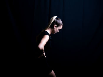 Side view of young woman standing against black background