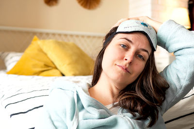 Middle aged woman in pajamas and sleep mask sitting relaxed on bed at home