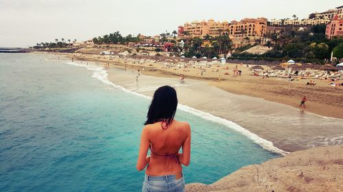 Rear view of shirtless woman standing at beach