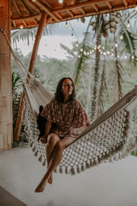 Woman sitting on hammock against palm trees