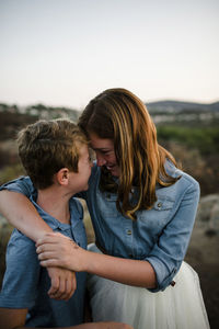 Playful siblings touching foreheads while standing on field during sunset