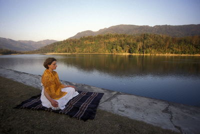 Woman mediating at lakeshore against sky