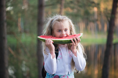 Girl eating watermelon while standing against lake