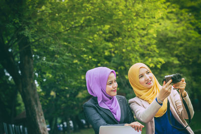 Female friends using camera while sitting at park